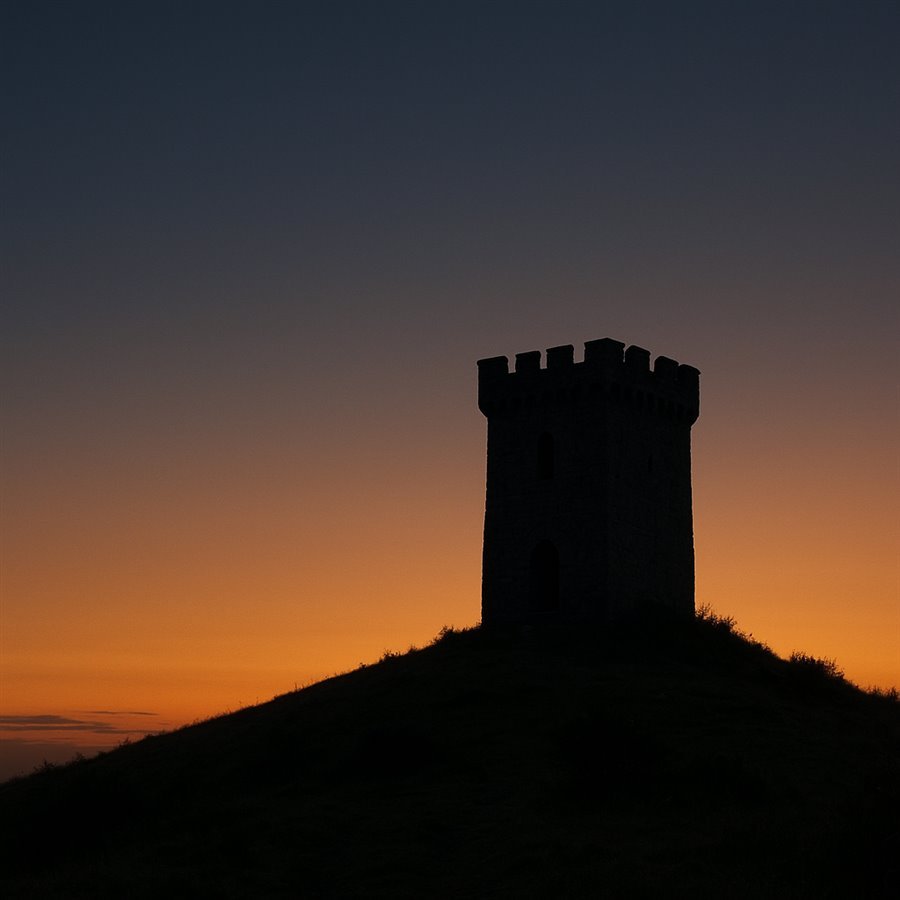 Uma antiga torre de vigia de pedra num morro, em silhueta contra a primeira luz dourada do amanhecer